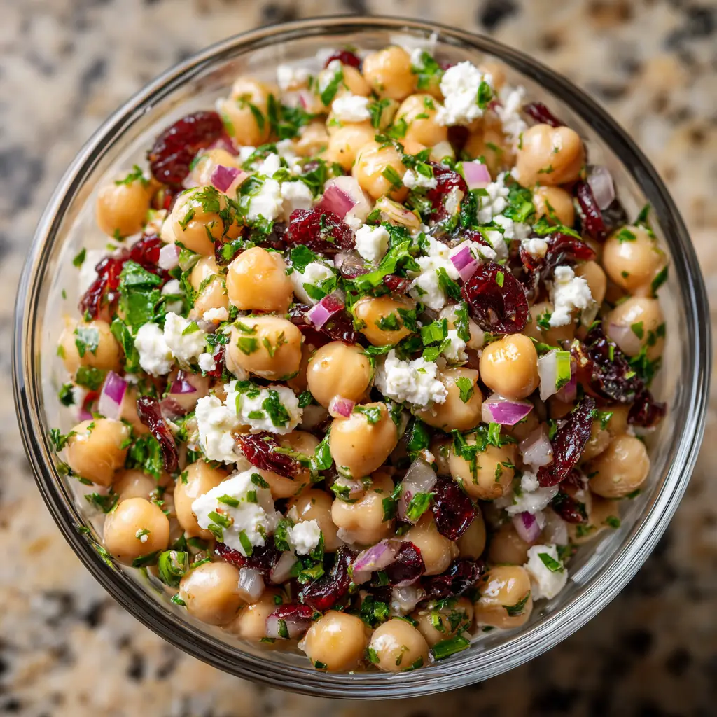 A spoonful of creamy chickpea salad being lifted from a bowl, showing the texture of the mashed chickpeas, feta, and cranberries.