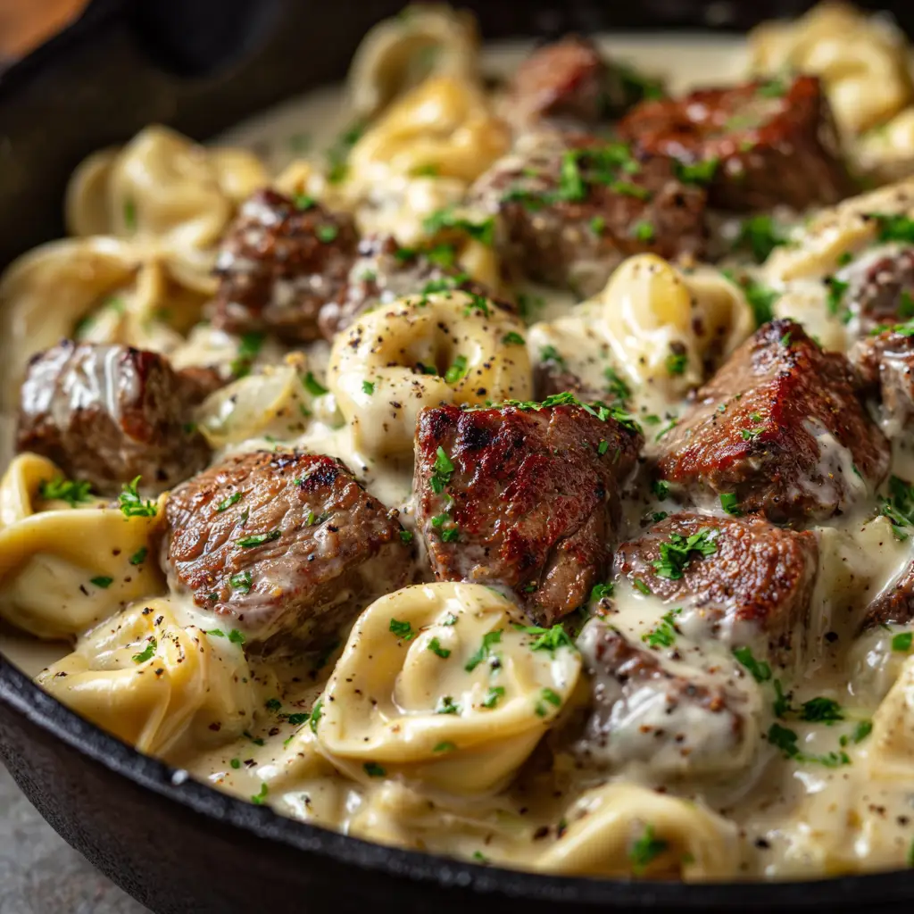 A fork lifting a piece of garlic butter steak with cheese tortellini from a bowl, showcasing the finished dish ready to be eaten.
