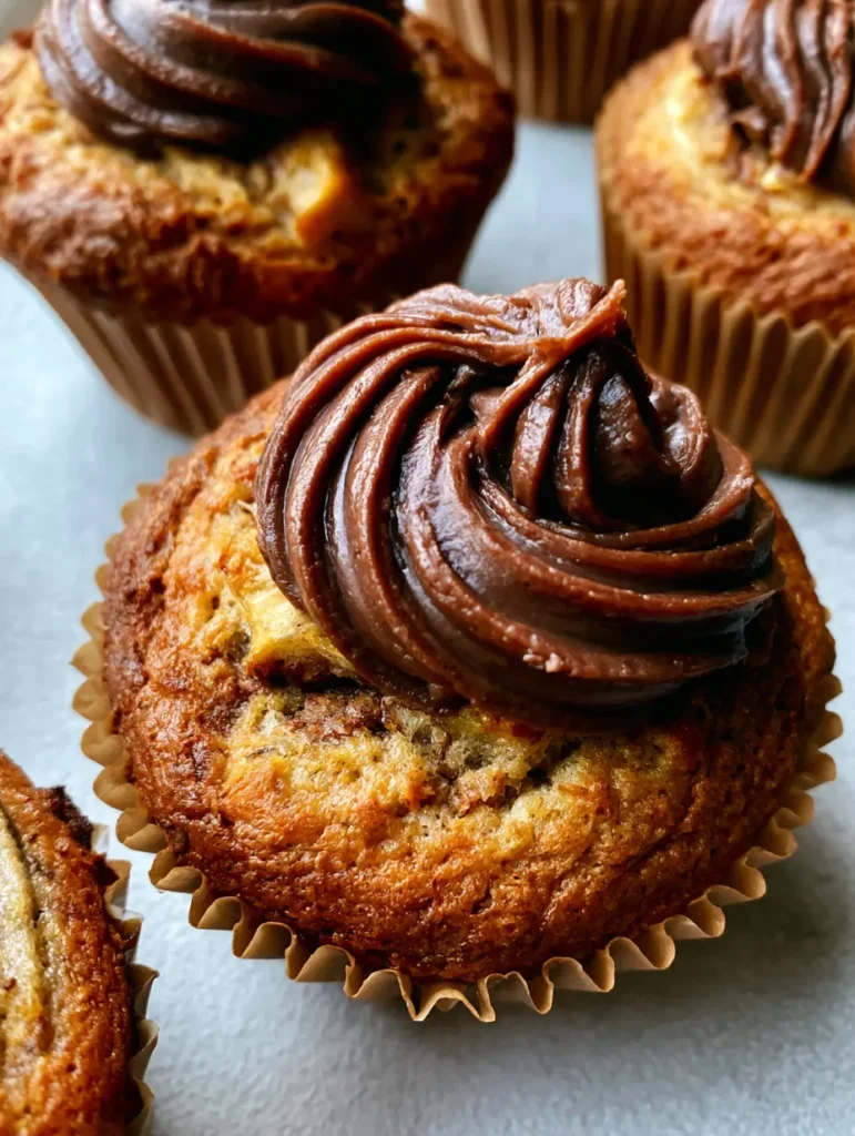 Mehrere Nutella-Bananen-Muffins auf einem neutralen grauen Hintergrund, die das goldbraune Backergebnis zeigen.