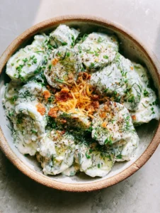 Draufsicht auf einen Ranch-Gurkensalat mit dicken Scheiben, weißem Dressing und Kräutern.