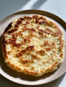 Ein hausgemachtes Hüttenkäse Fladenbrot in der Hand gehalten, weiche Textur und goldbraune Blasen sichtbar.