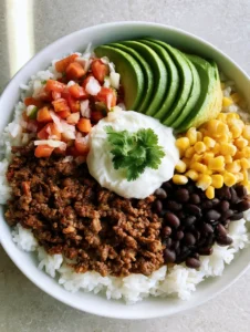 Nahaufnahme einer Taco-Bowl mit Hackfleisch, Pico de Gallo und einem Klecks saurer Sahne von oben.