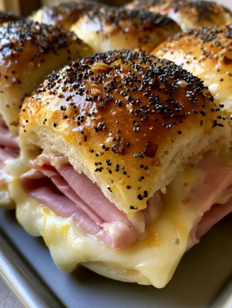 Schinken-Käse-Slider: Das ultimative Rezept für goldbraune Party-Brötchen 2 Nahaufnahme von Schinken-Käse-Slidern auf einem Backblech, Fokus auf den geschmolzenen Schweizer Käse und die glänzende Glasur.