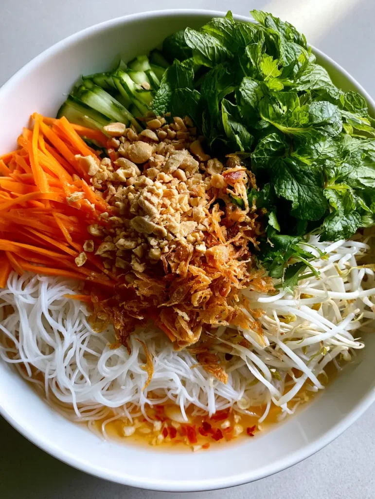 Nahaufnahme eines Vietnamesischen Nudelsalats mit frischer Minze, Koriander und goldbraunen Röstzwiebeln.