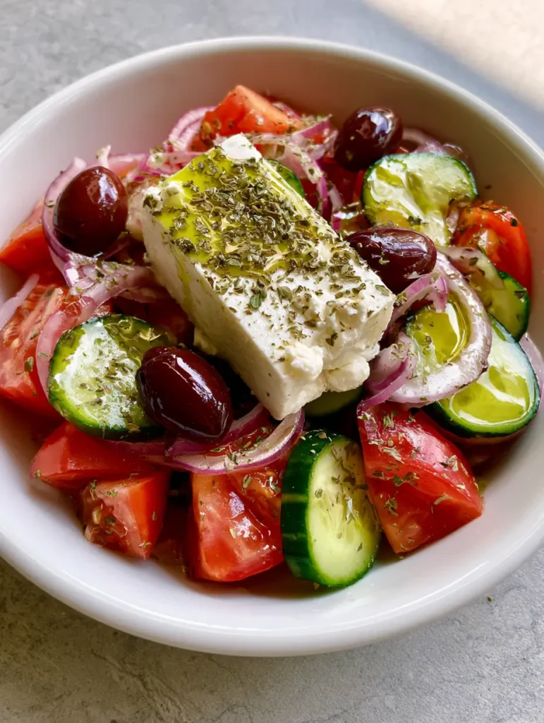 Griechischer Salat: Das ultimative Rezept für authentischen Horiatiki 1 Ein dicker Block Feta-Käse auf einem Bett aus mediterranem Gemüse, übergossen mit Olivenöl.