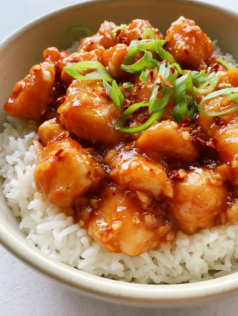 Portion Thai Hähnchen süß-scharf auf fluffigem Reis mit sichtbaren Chiliflocken und Frühlingszwiebeln.