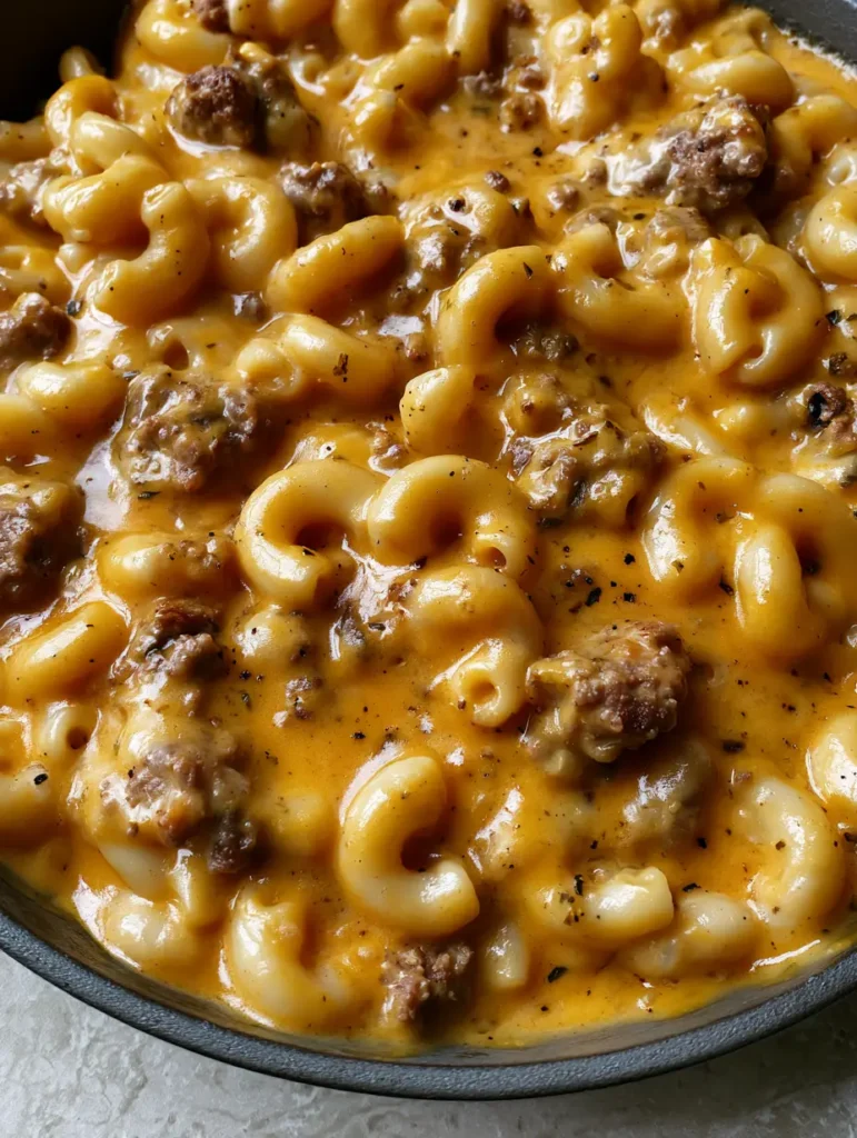 Rustikale gusseiserne Pfanne gefüllt mit Nudeln, Hackfleisch und Cheddar-Sauce auf grauem Steinuntergrund.