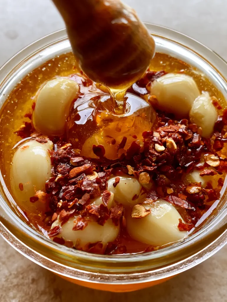Scharfer Honig Rezept: Der ultimative Hot Honey mit Knoblauch und Chili 1 Handgehaltenes Smartphone Foto von bernsteinfarbenem Honig mit Chilisamen und Knoblauchzehen, Scharfer Honig Rezept.